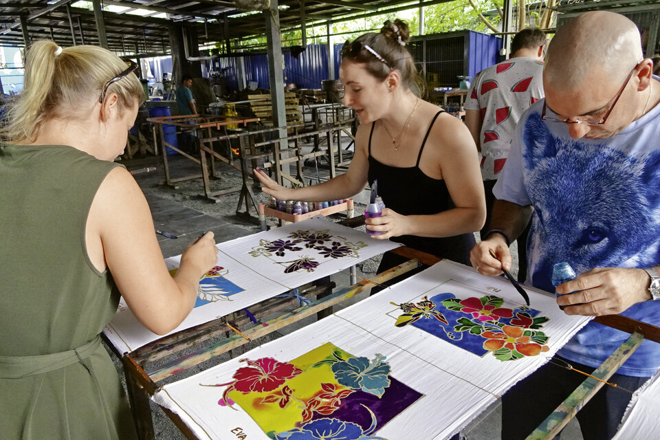 Abb. 10: Tourist:innen versuchen sich unter fachkundiger Anleitung  in der Penang Batik Factory im traditionellen Batik-Kunsthandwerk.
